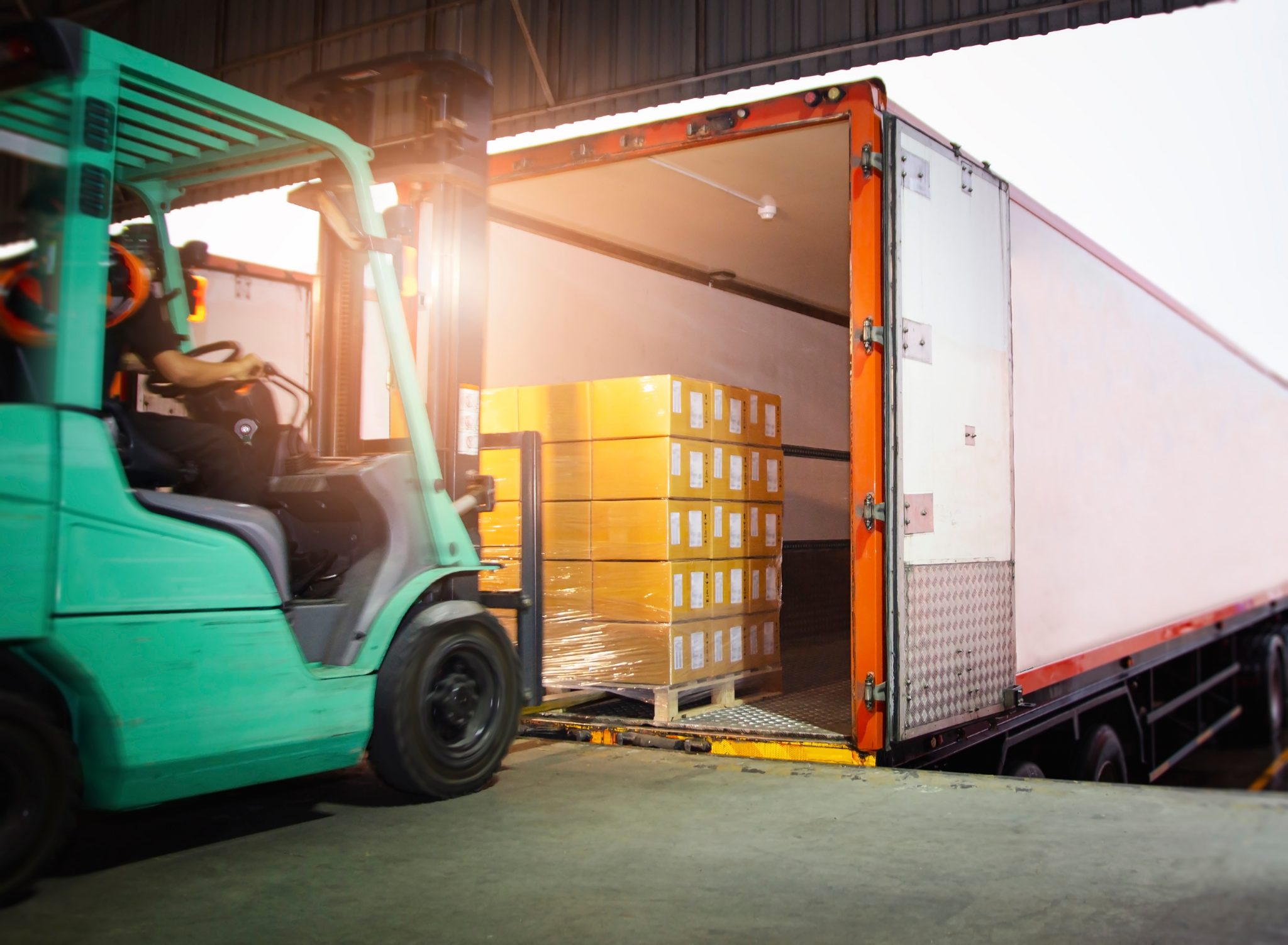 Green forklift loading trailer at warehouse dock.