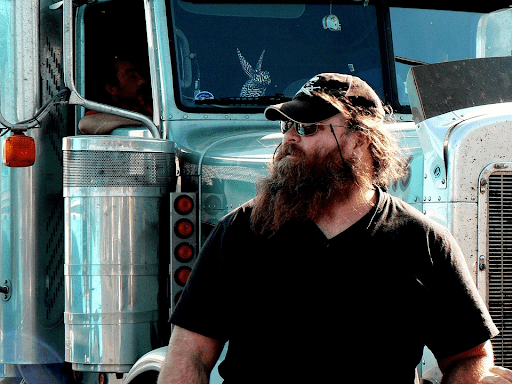 Truck Driver leaning against his truck while waiting in Warehouse Yard.